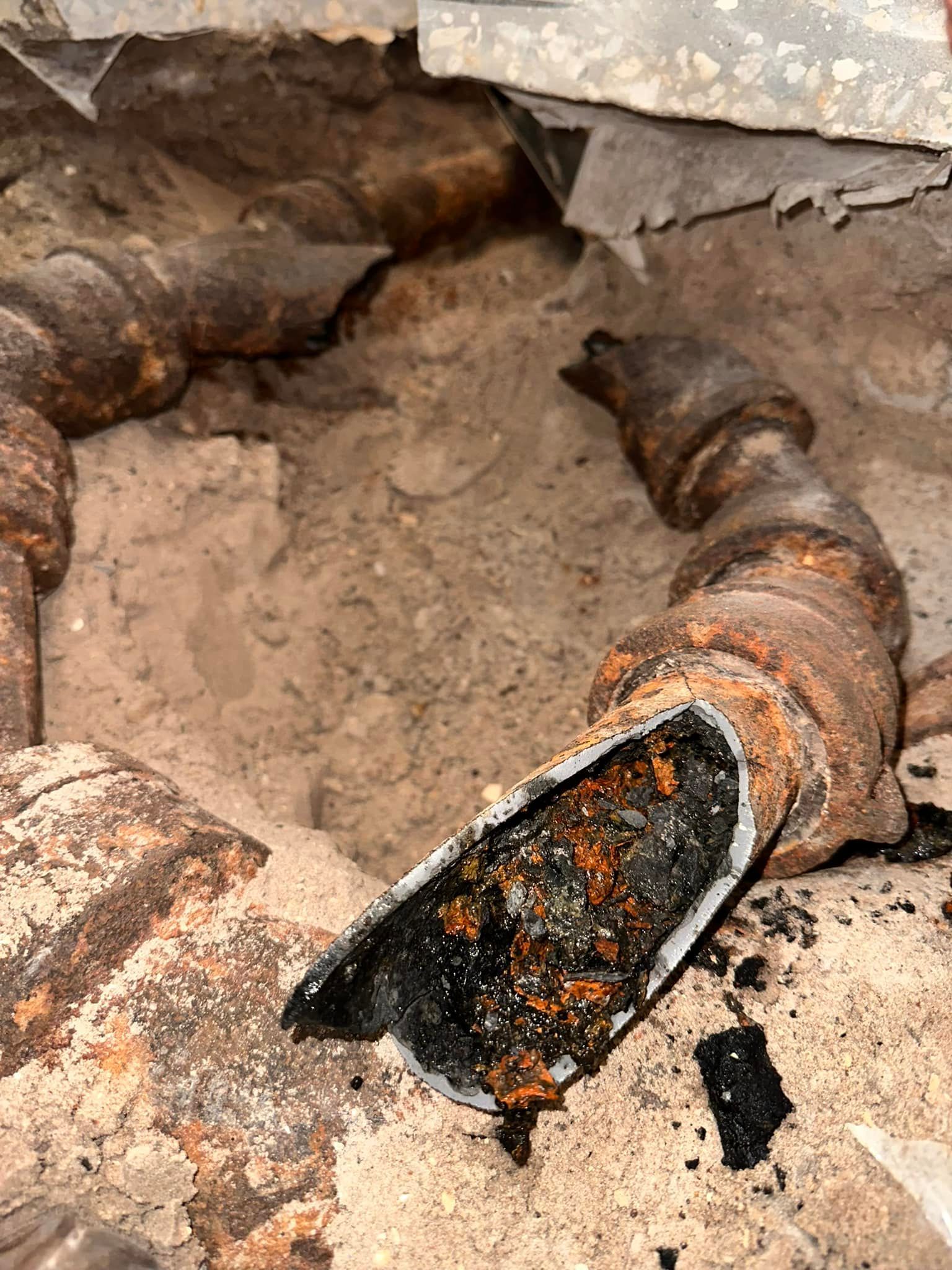 Corroded, broken cast iron pipe in sandy soil, revealing a dark interior.