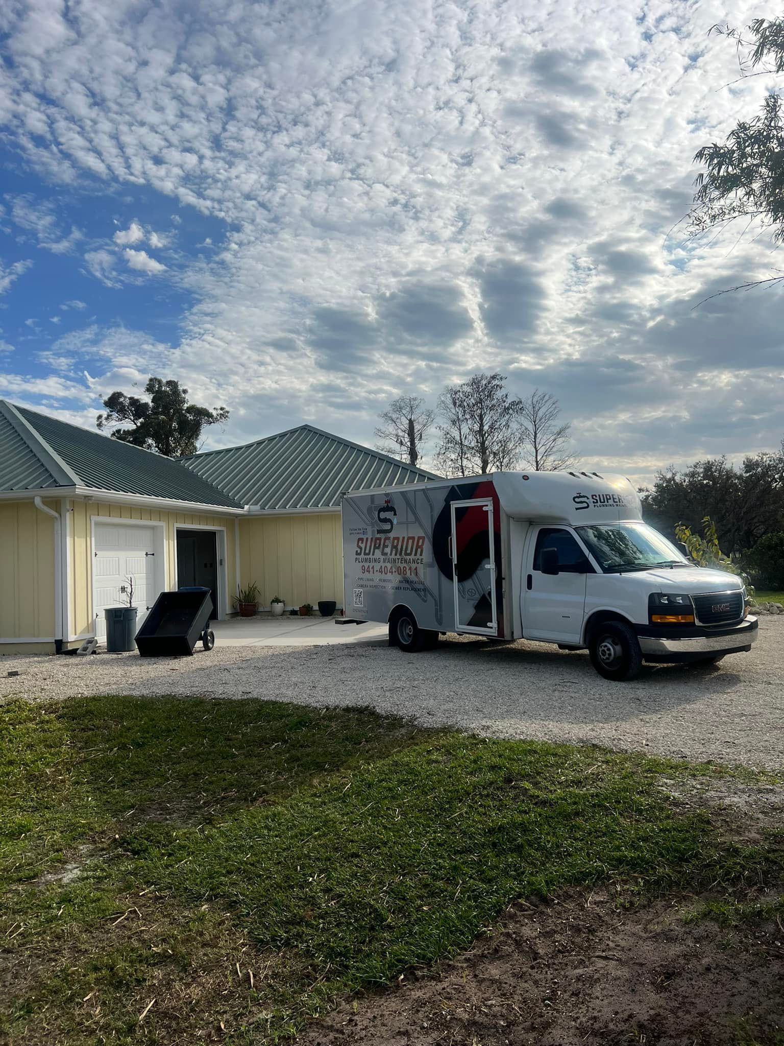 White van parked in front of a yellow building with green roof, against a cloudy sky.