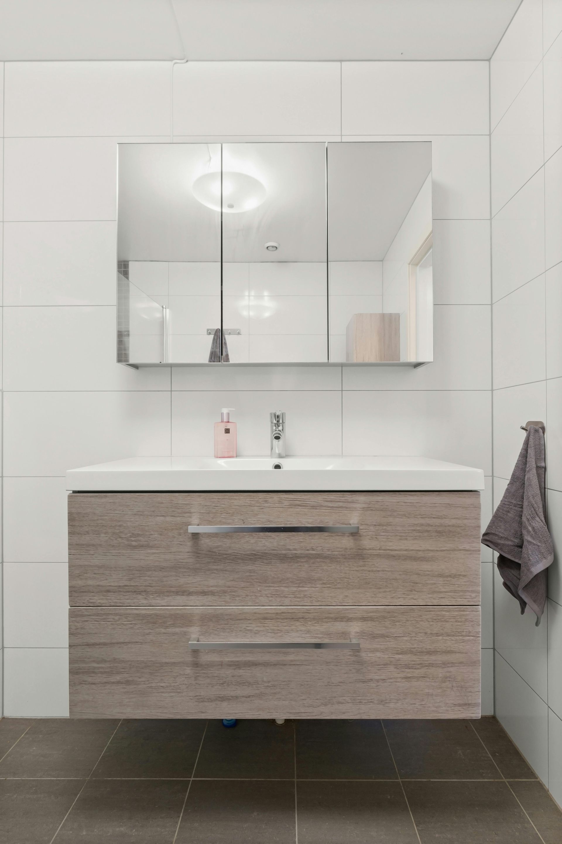 Bathroom with wood-grained vanity, large mirror, and white tiled walls. A towel hangs on the right.