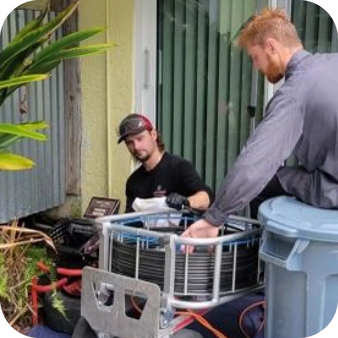 Two men working on equipment outdoors. One looks at a screen, other handles a blue-trimmed metal cage.