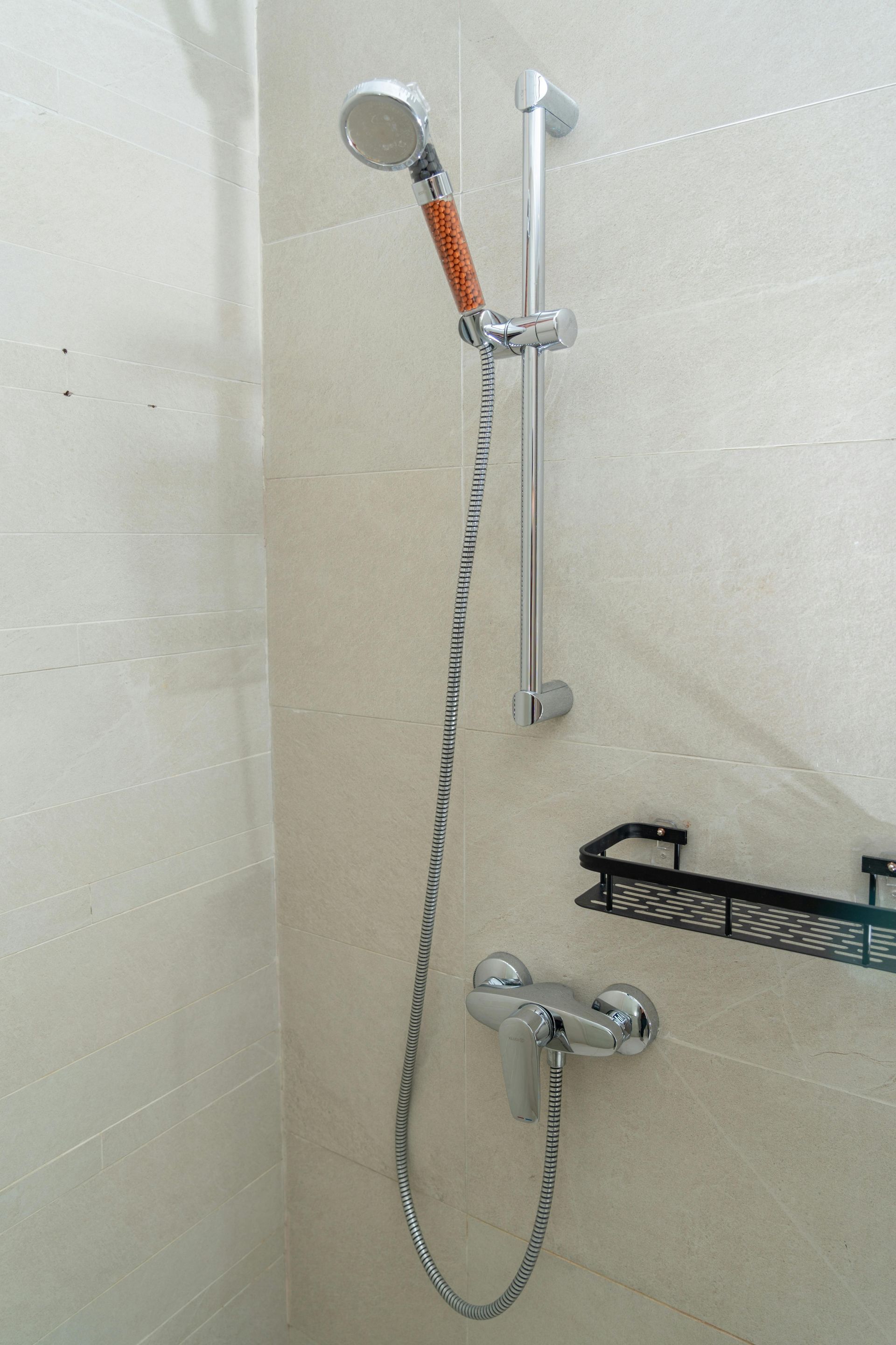 Chrome showerhead on a vertical bar with a metal hose, mounted on light-colored tile.