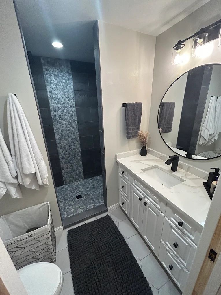 Bathroom with walk-in shower, white vanity, black accents, gray walls, and a round mirror.