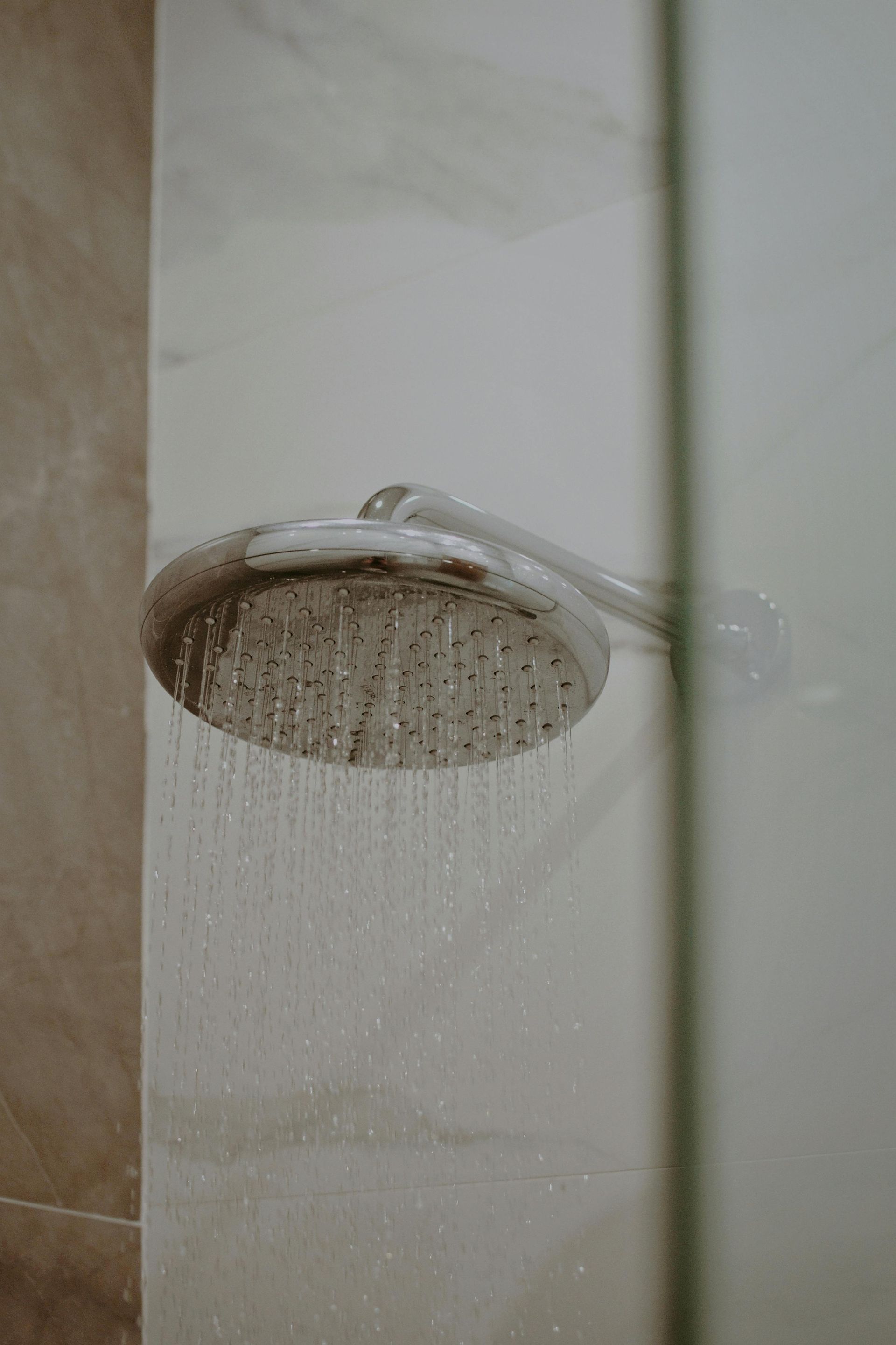 Shower head with water spraying against a light-colored tiled wall.