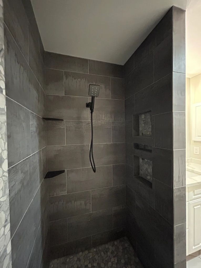 Dark tiled shower with built-in shelves and niches, gray pebble floor, and a showerhead.