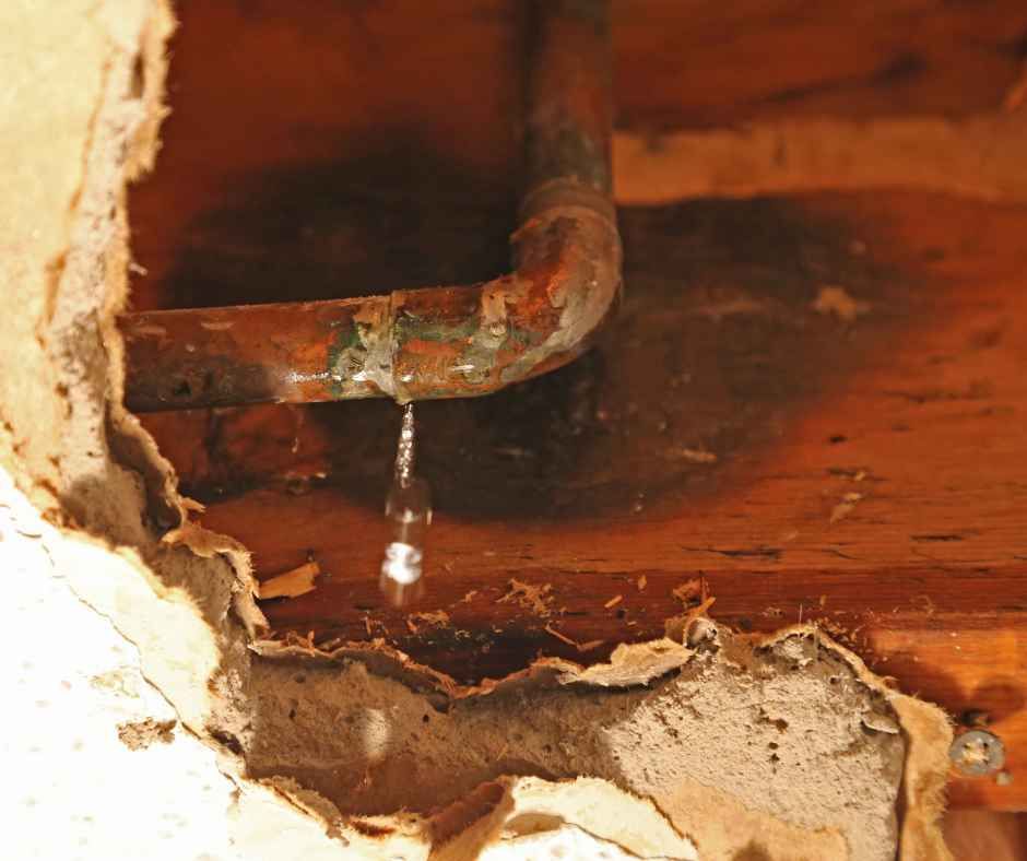 A copper water pipe leaking water, inside damaged wall.