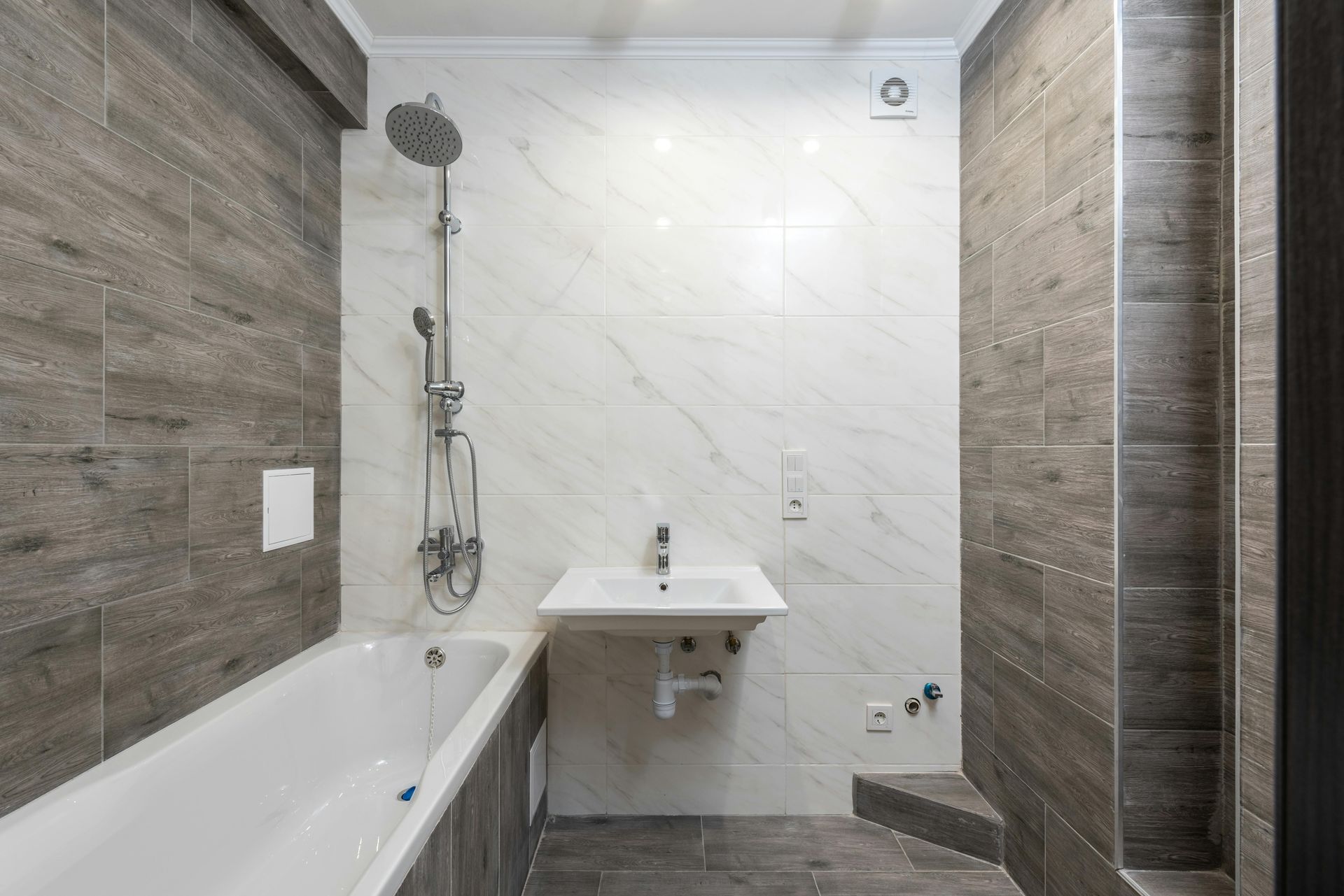 Bathroom with white tub, sink, and showerhead, gray and white tile walls.