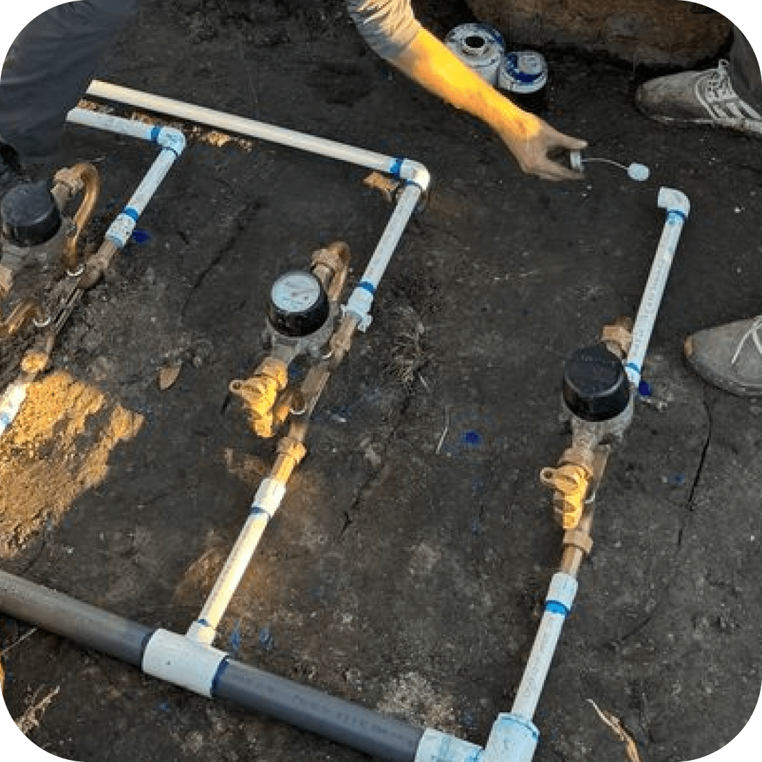 Irrigation system components laid out on the ground: pipes, valves, gauges, and a person working.