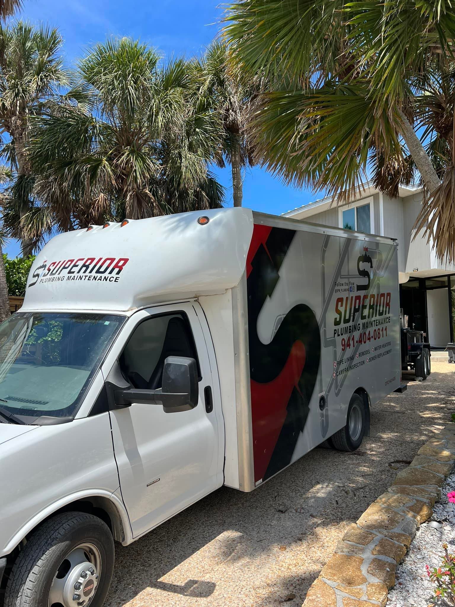 A white Superior box truck parked on a gravel driveway under palm trees and a bright blue sky.