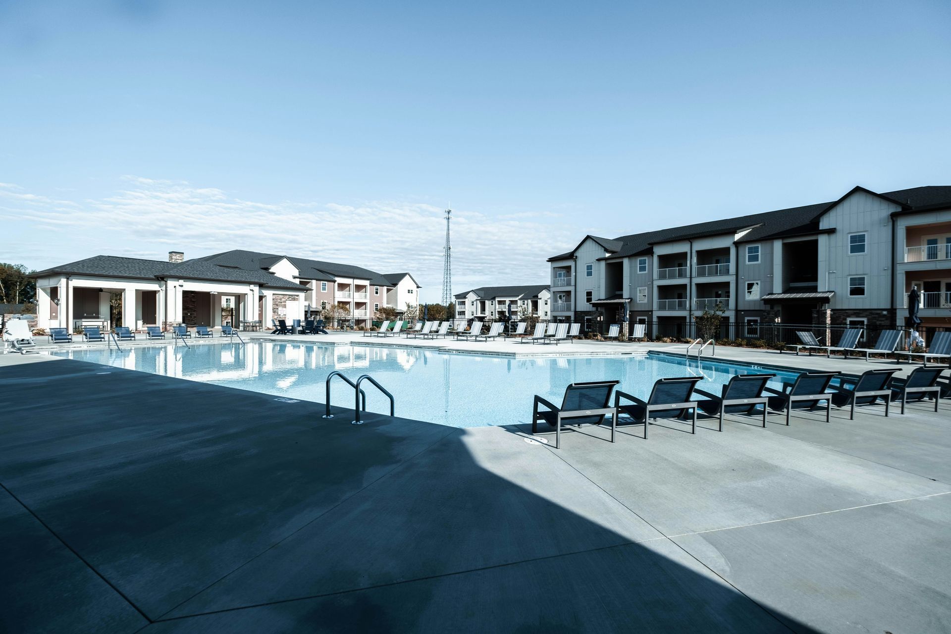 A swimming pool at an apartment complex, with lounge chairs on the deck and modern residential buildings in the background.