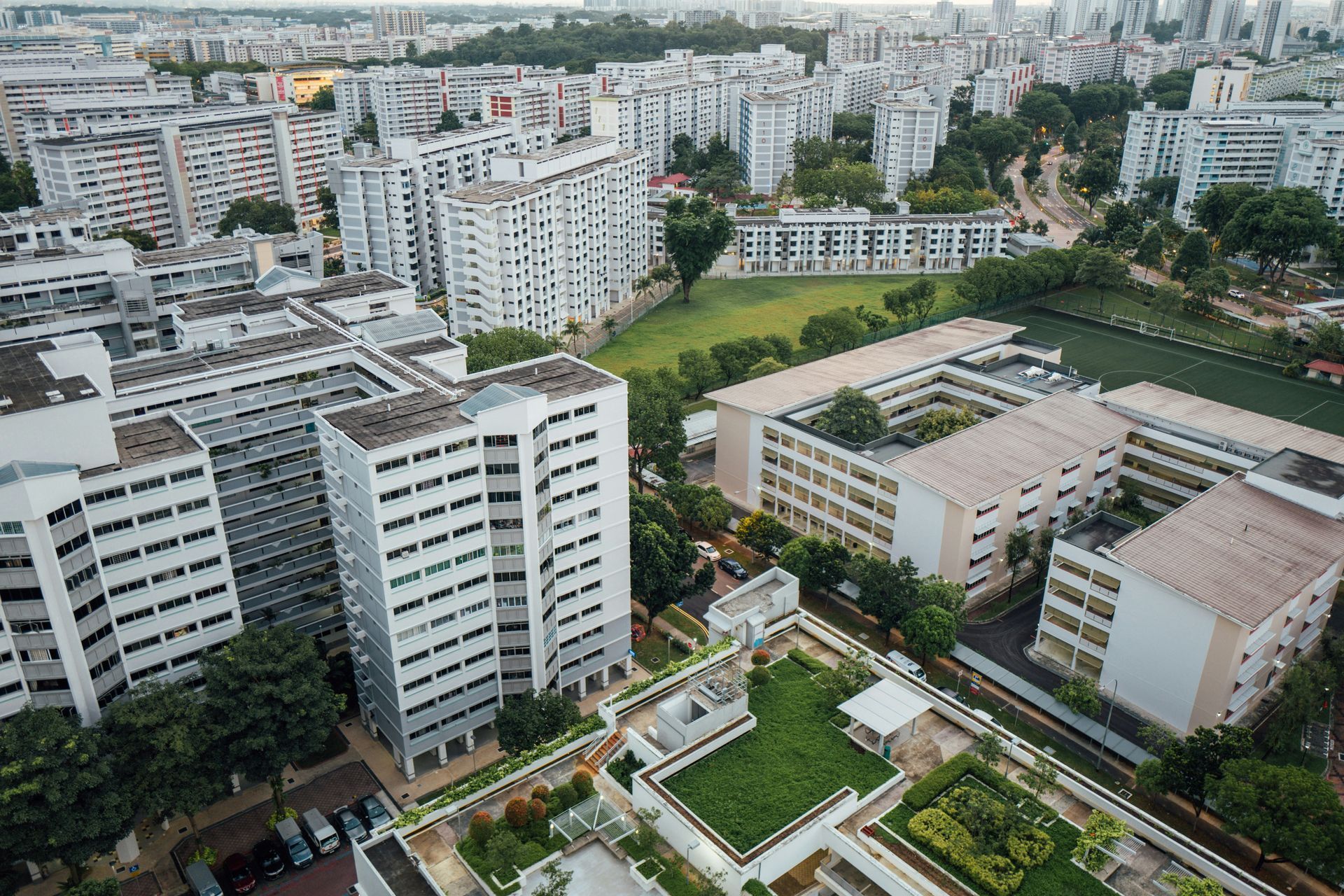 An aerial view of high-rise residential apartment buildings in a city, surrounded by trees and green rooftop garden spaces.