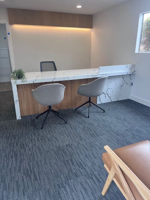 Modern reception area with marble-look counter, wood paneling, gray chairs, and carpet.