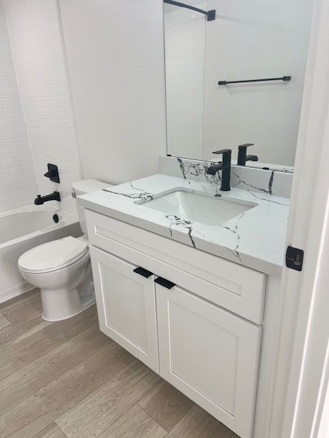 Bathroom with white vanity, black fixtures, and light floor. A toilet, bathtub, and mirror are visible.