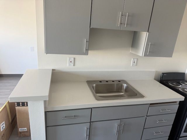 Gray kitchen cabinets with a white countertop and a stainless steel sink.