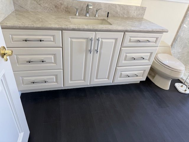 White bathroom vanity with drawers and doors, tan countertop, dark flooring.