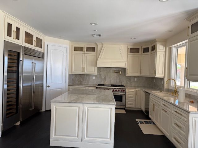 Cream-colored kitchen with stainless steel appliances, white cabinetry, marble countertops, and a central island.