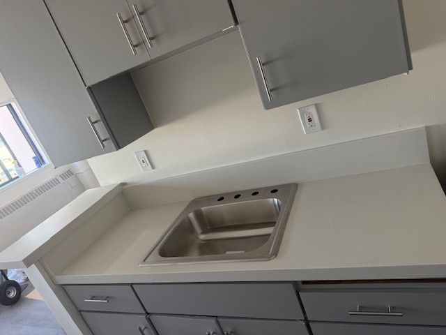 Gray kitchen cabinets and countertop with a stainless steel sink.