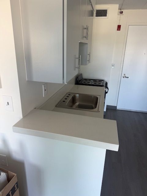 Small white kitchen with a sink, stove, and cabinets; gray countertop and flooring.