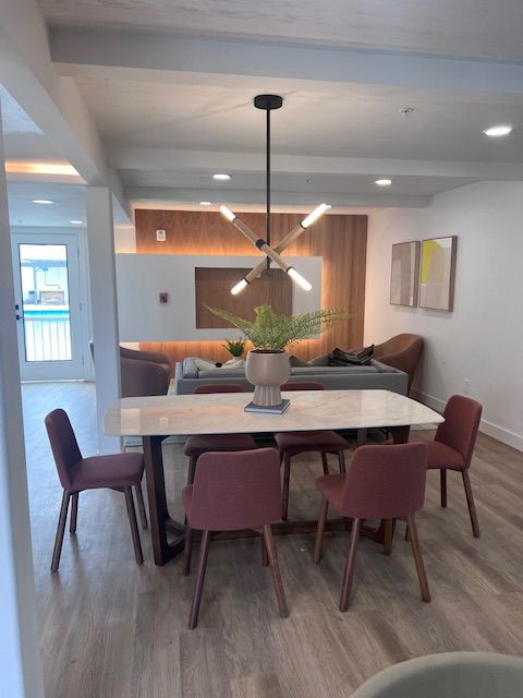 Dining room with marble table, burgundy chairs, chandelier, and wood-paneled wall with living room visible beyond.