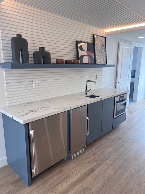 Kitchenette with blue cabinets, marble countertop, stainless steel appliances, and shelf with decor.