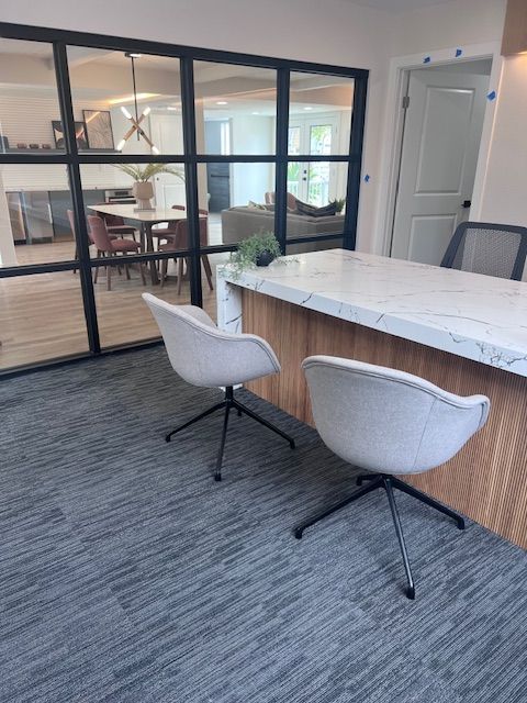 Two gray swivel chairs at a kitchen island with a marble countertop, and a glass wall.