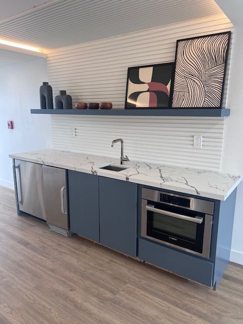 A small kitchen area with a built-in refrigerator, cabinets, sink, microwave, and a shelf with decor.