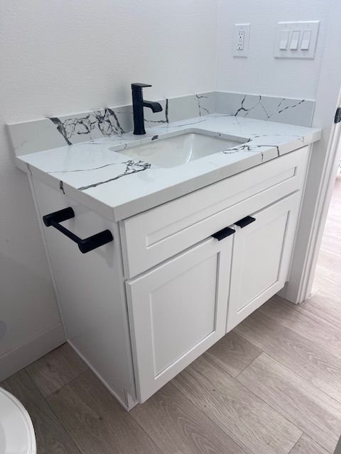 White bathroom vanity with marble-look countertop, black faucet and hardware, set against a white wall.