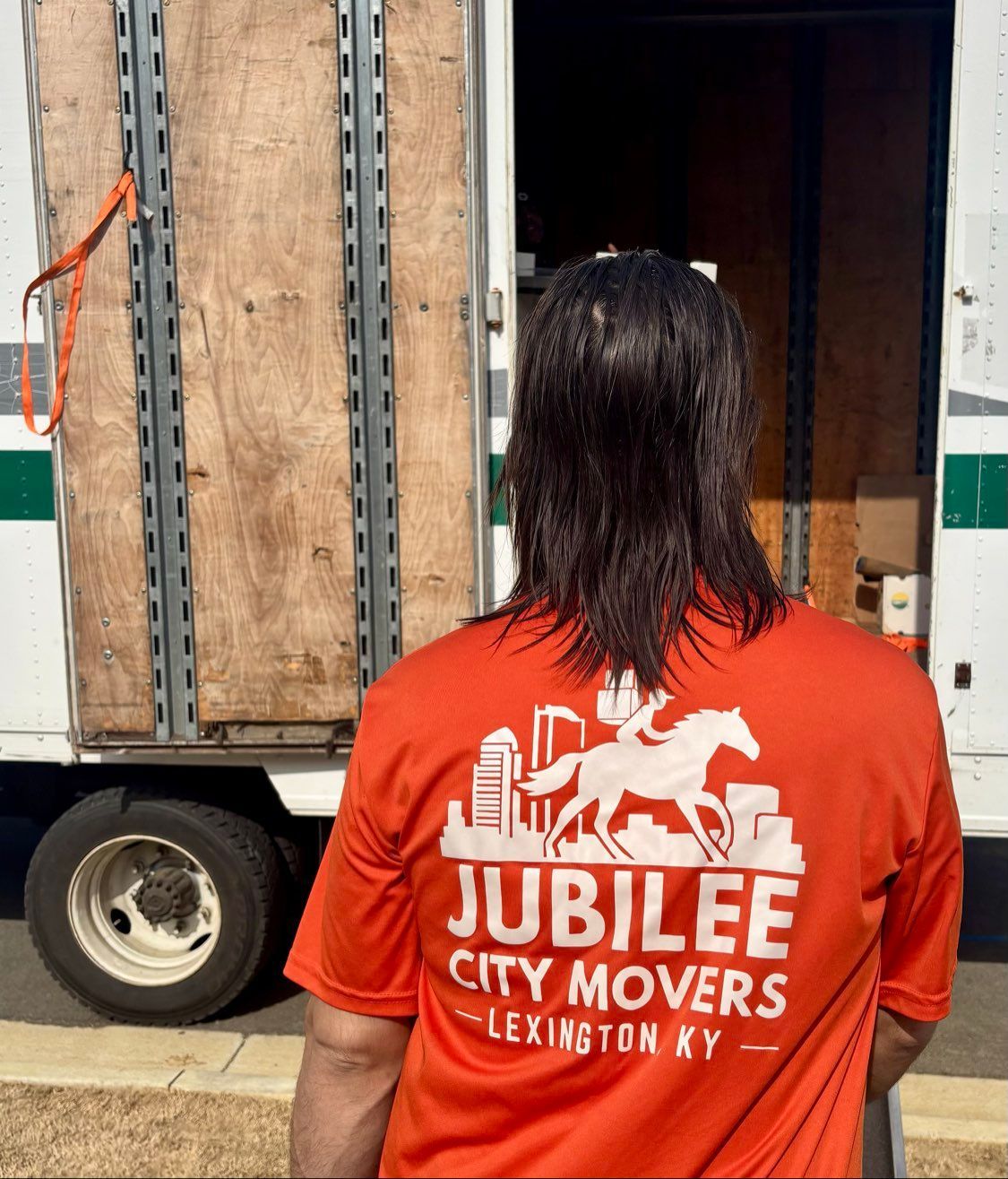 Person in an orange Jubilee City Movers shirt standing by a moving truck