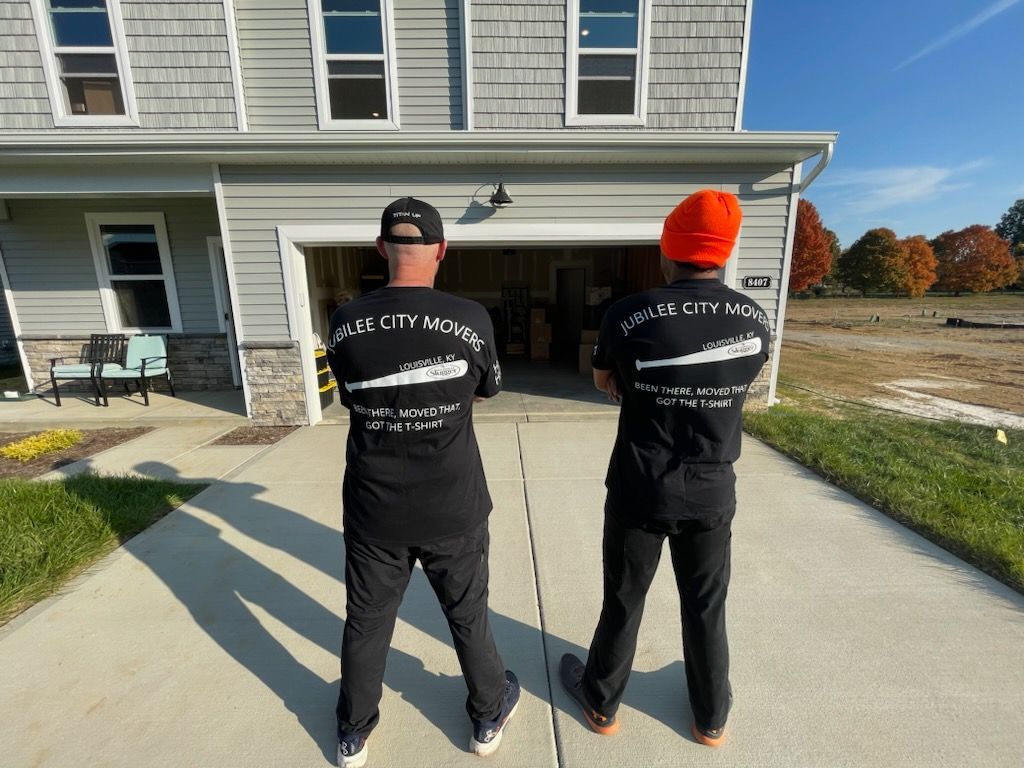 Two people in black shirts and pants stand outside a house, facing an open garage