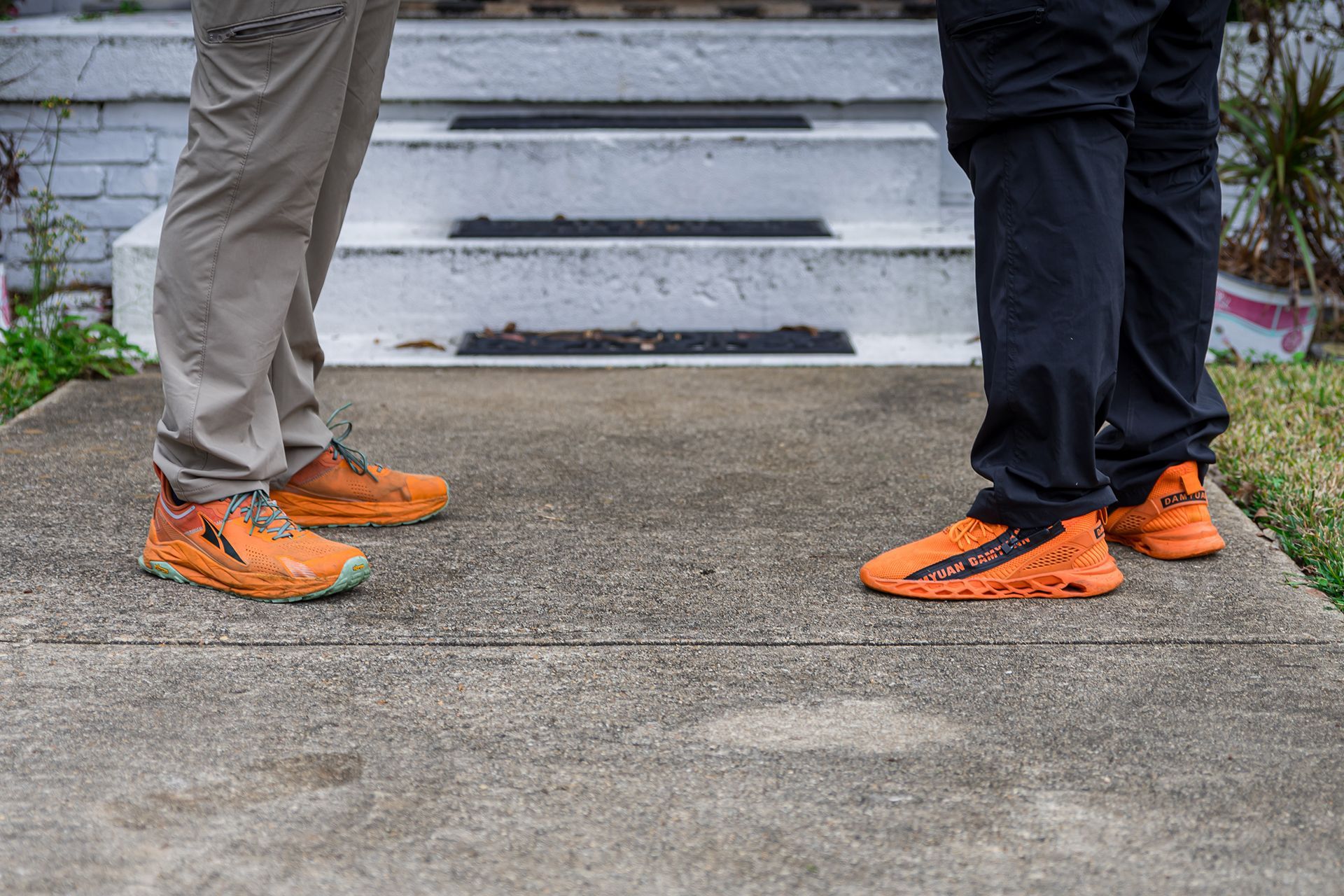 Two people wearing bright orange shoes stand on a sidewalk in front of steps