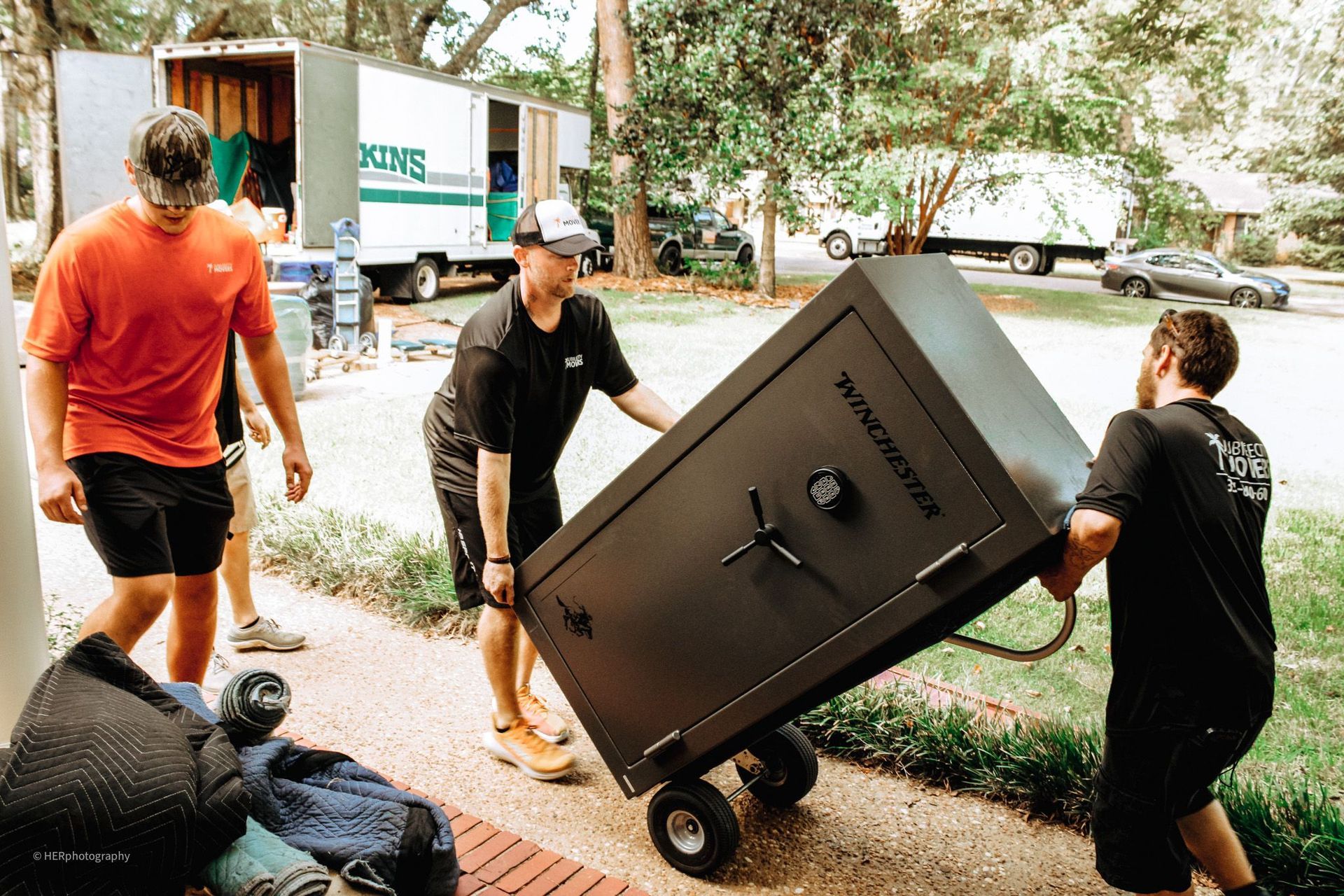 People moving a large dark safe on a wheeled cart outside a building
