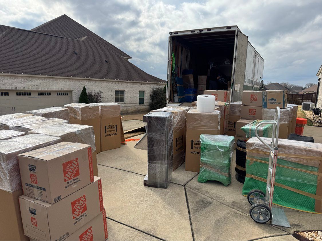 Boxes and household items stacked outside a moving truck on a driveway near a house