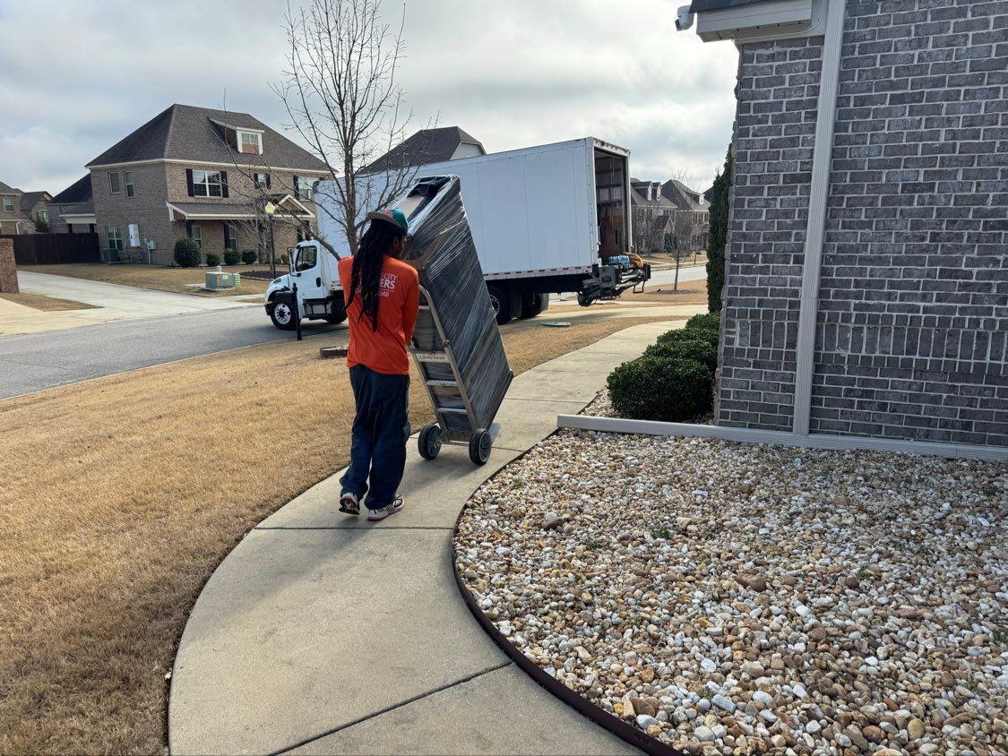 Man pushing a large panel along a curved sidewalk in a suburban driveway area