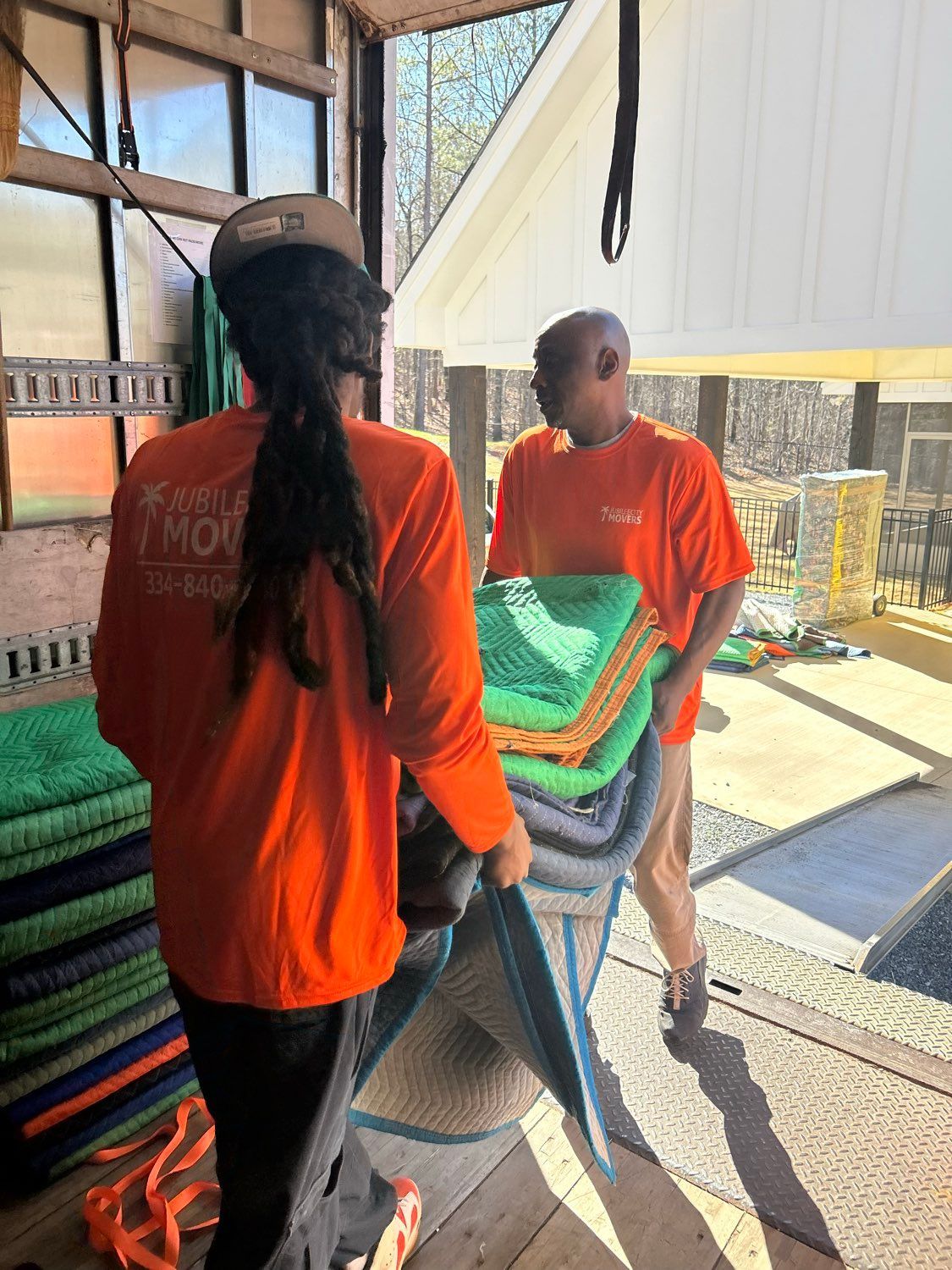Two people in orange shirts carry folded mats 