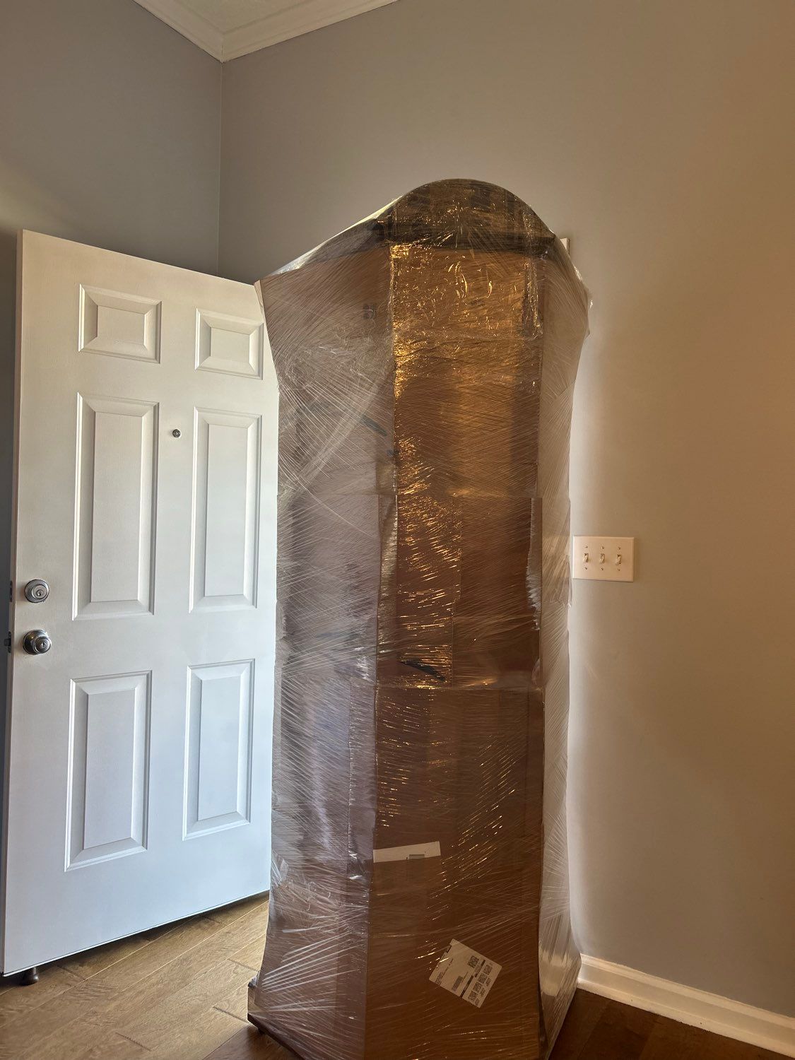 Tall plastic-wrapped package standing upright in a room
