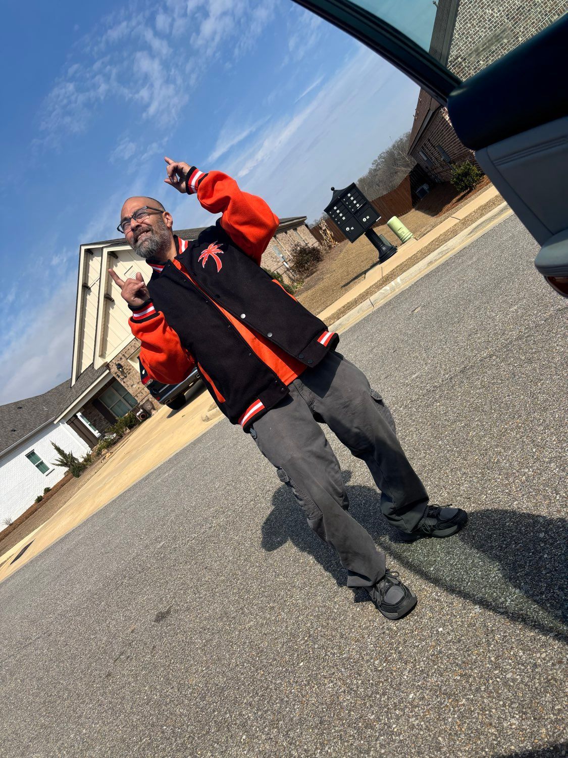 Person in a black and orange jacket standing outdoors on a sunny street