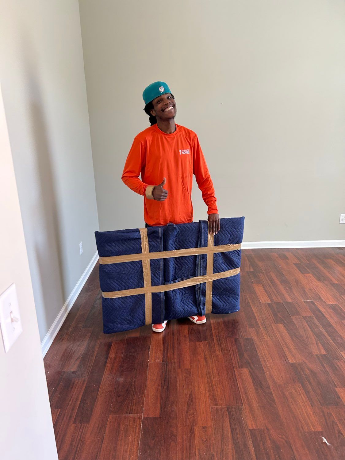 Smiling man in an orange shirt holding a large wrapped blue package 