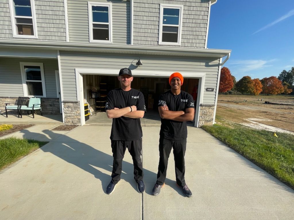 Two people in black outfits stand in a driveway in front of a house