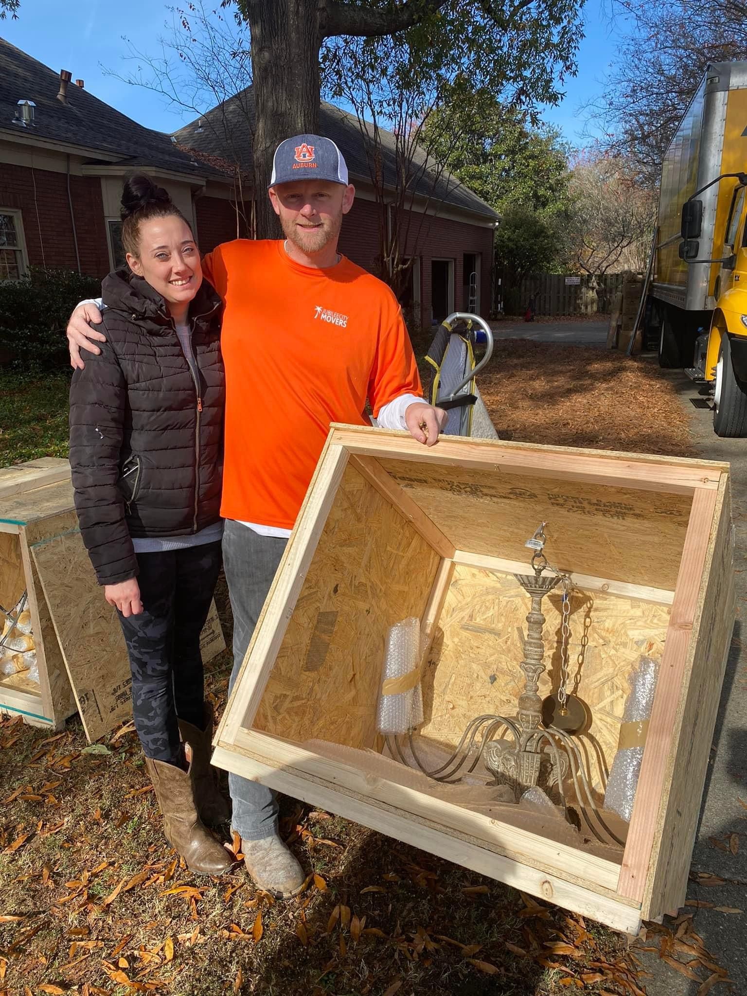 Two people outdoors holding a box that has a chandelier inside it
