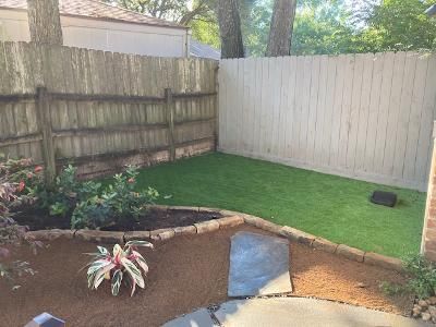 Backyard with a brown mulch bed, green lawn, and wooden fences.