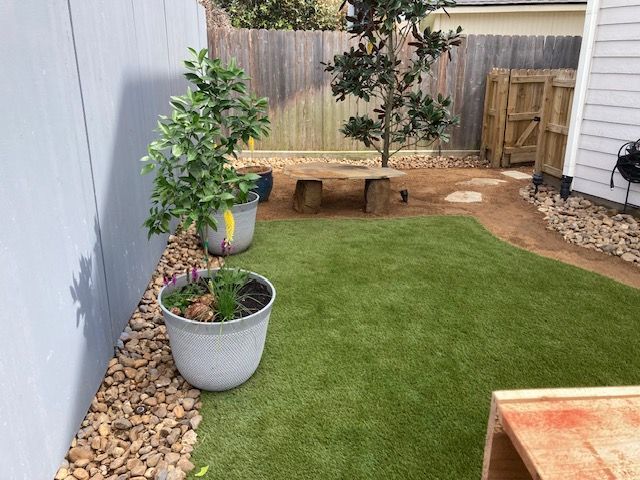 Backyard with artificial grass, plants in pots, gravel border, wooden fence and bench.