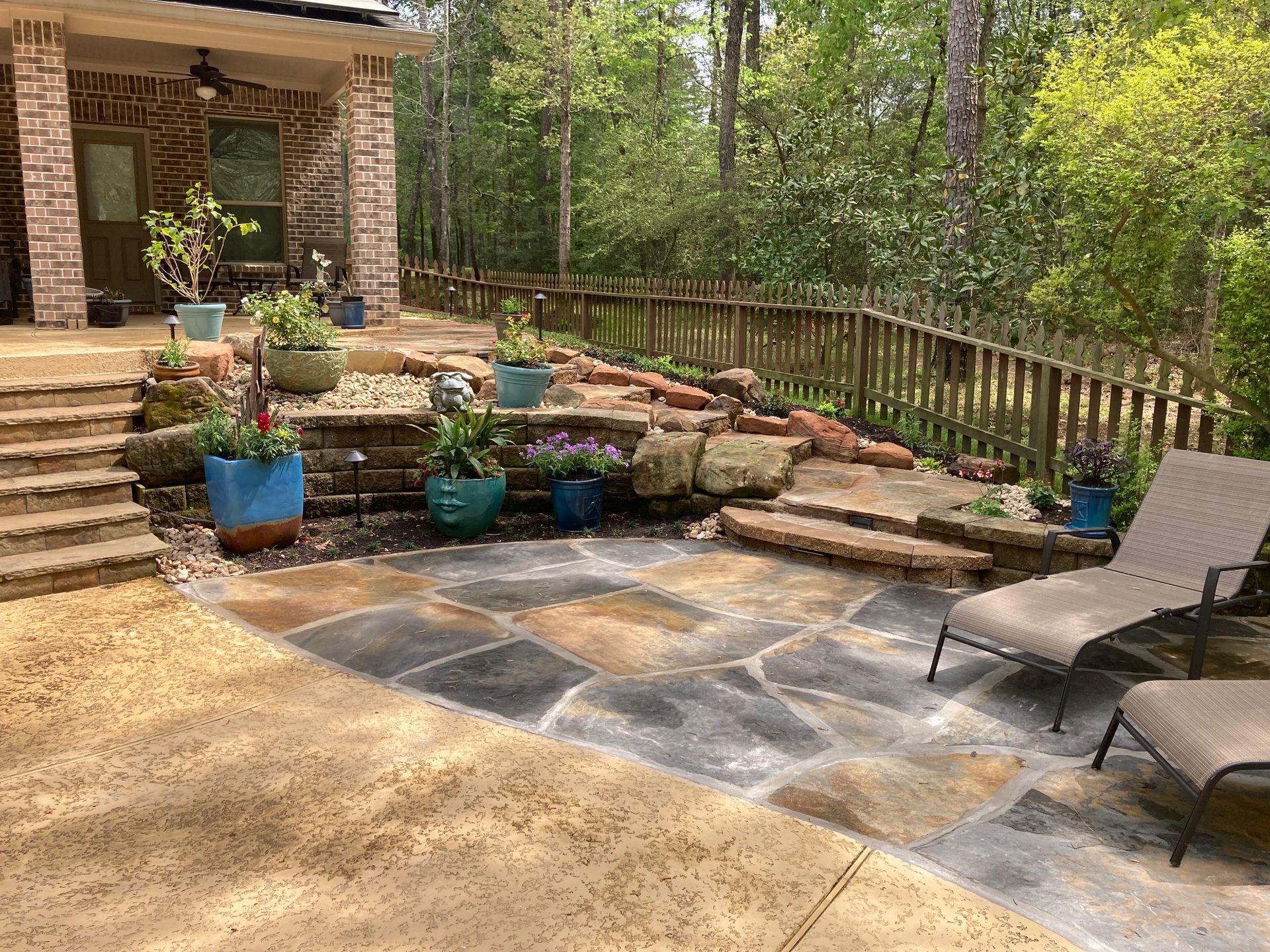 Patio with flagstone and concrete, tiered landscaping with potted plants, and two lounge chairs.
