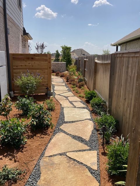 Flagstone path between fences and landscaping on a sunny day.