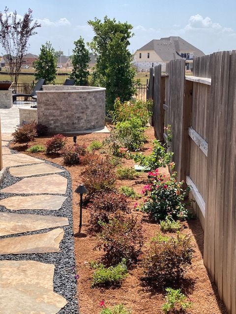 Flagstone path leads through a landscaped yard with a wood fence and flower beds.