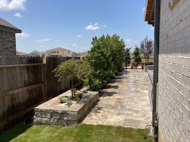 Backyard patio with stone pavers and retaining wall with trees and green grass.