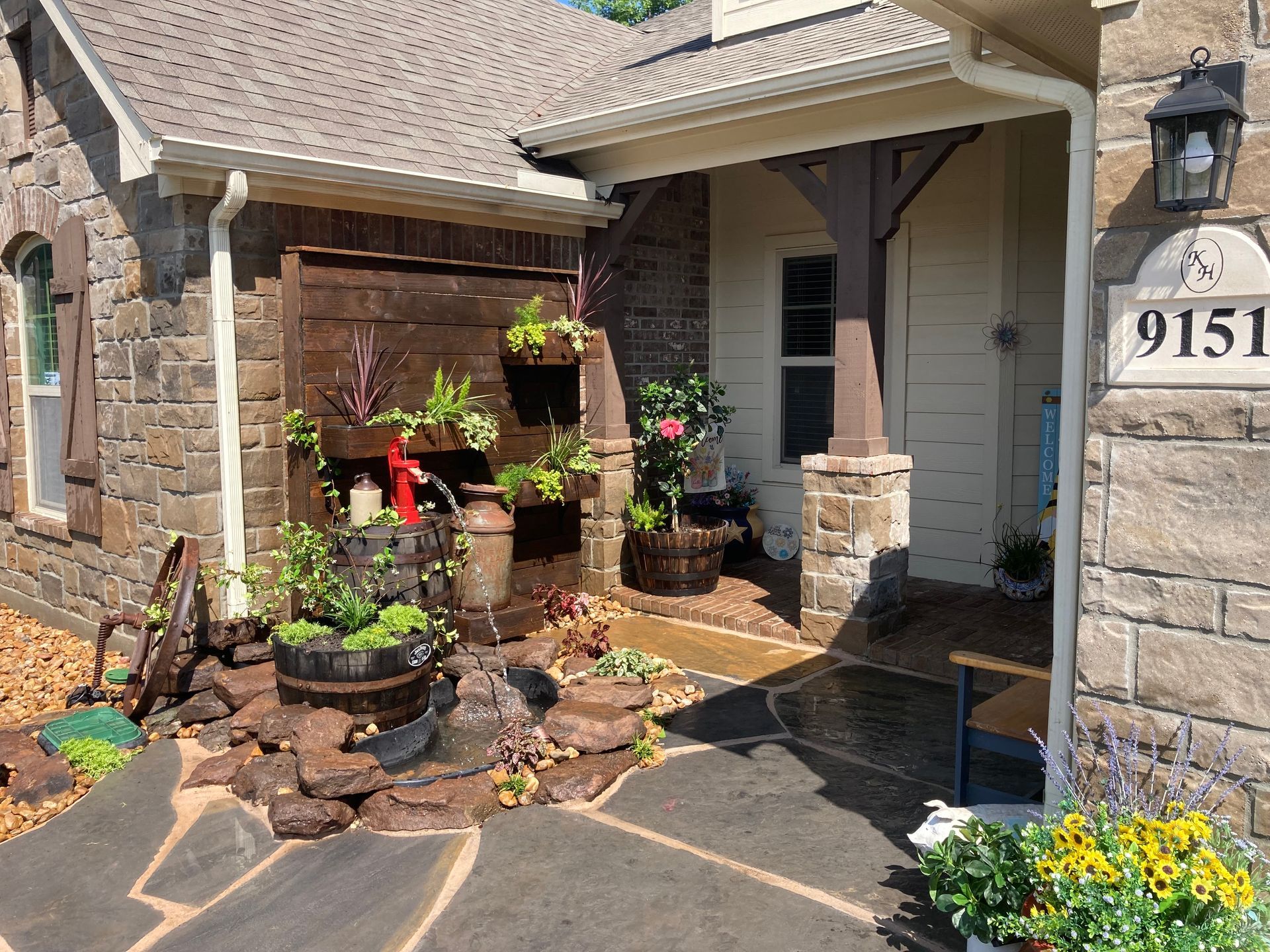 Stone facade of a house with decorative water fountain, wood accent wall, and potted plants.