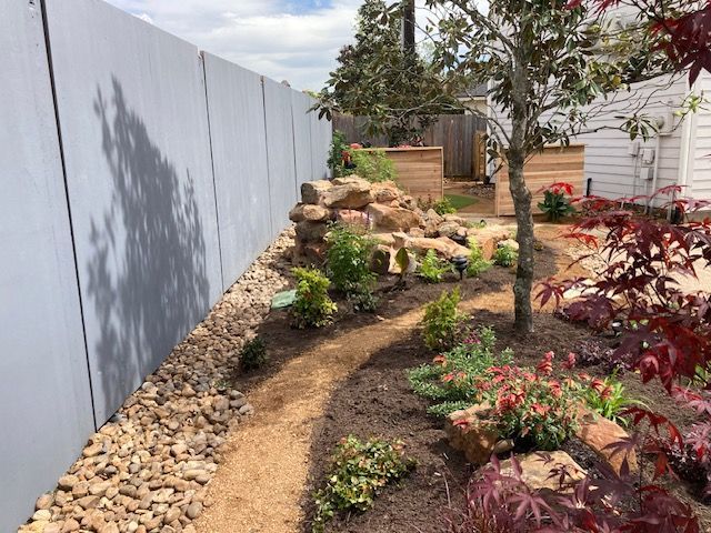 Landscaped backyard with gravel path, rock features, and tall gray fence.