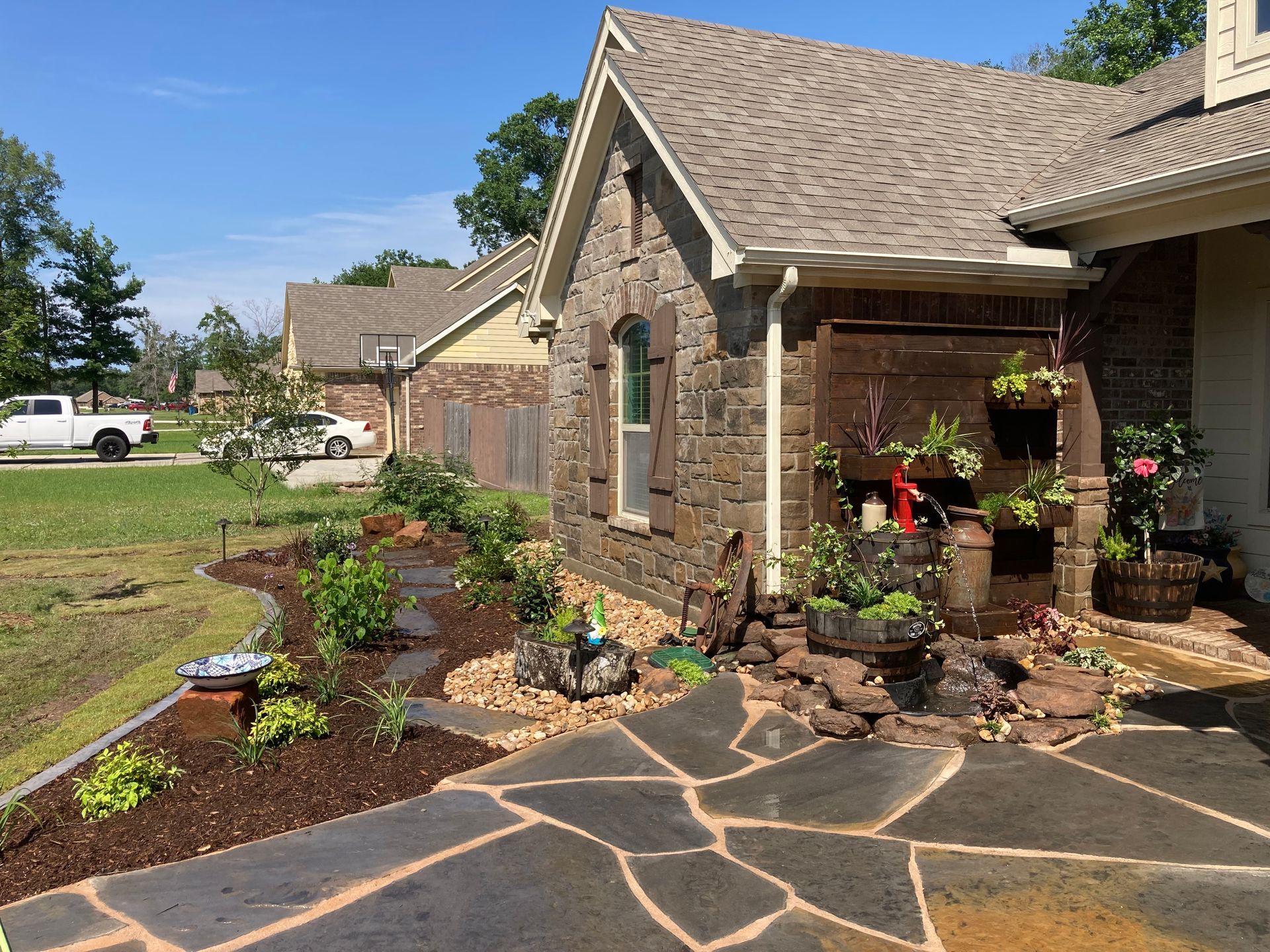 Stone house with a landscaped yard and flagstone walkway. Plants and flowers are arranged around the entrance.