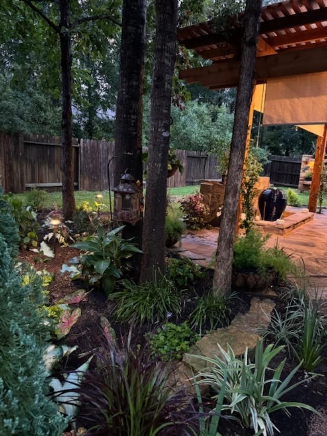 Backyard garden with trees, plants, stone pathway, and a patio with a pergola.