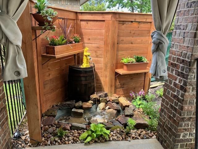 Outdoor corner water feature with wooden fence, plants, and barrel fountain.