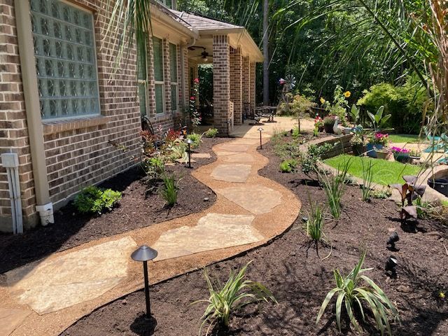 Stone pathway winds through landscaped yard toward a house with brick and a porch.